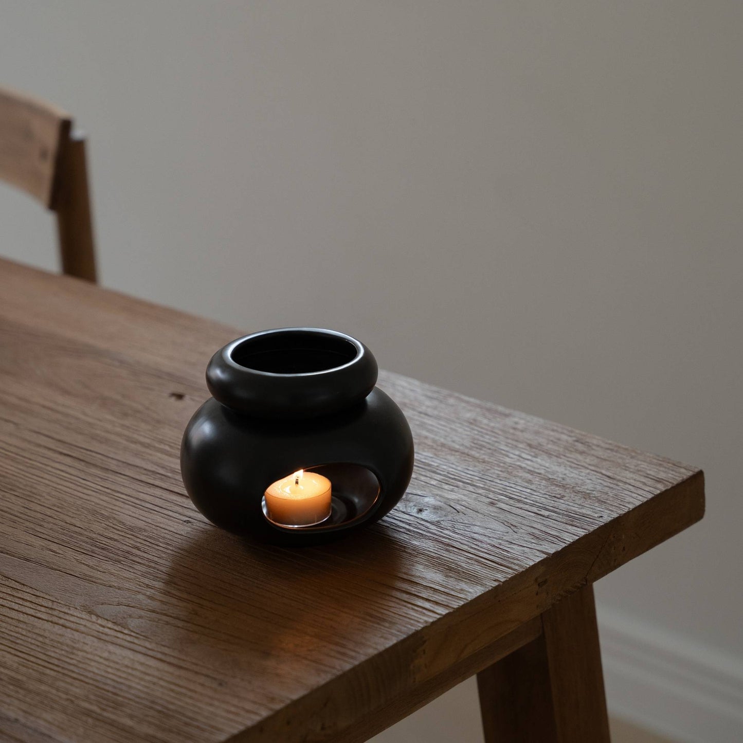 어두운 나무 테이블 위에 단독으로 놓인 블랙 조약돌 오일버너와 안에서 켜진 티라이트 캔들을 위에서 살짝 내려다본 제품 연출 사진