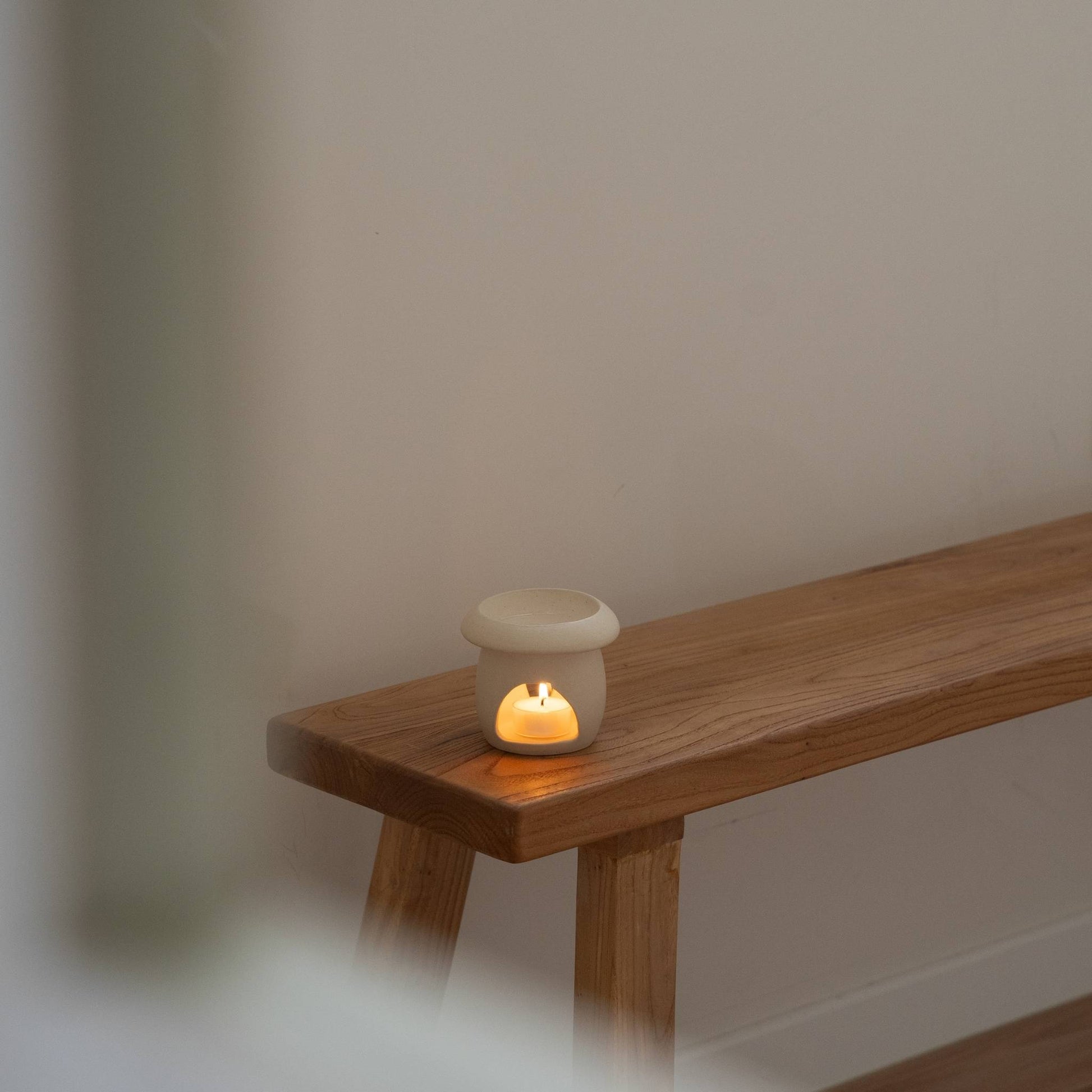 나무 벤치 위에 놓인 베이지 색 머쉬룸 오일버너와 안에서 켜진 티라이트 캔들 사진