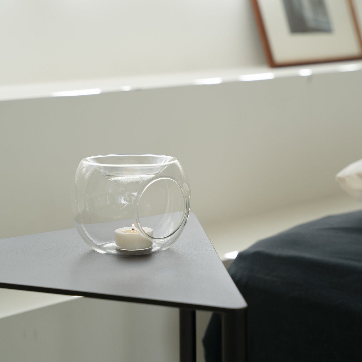 창가 옆 그레이 사이드테이블 위에 놓인 투명 유리 티라이트 홀더와 안에서 켜진 티라이트 캔들이 보이는 거실 연출 사진