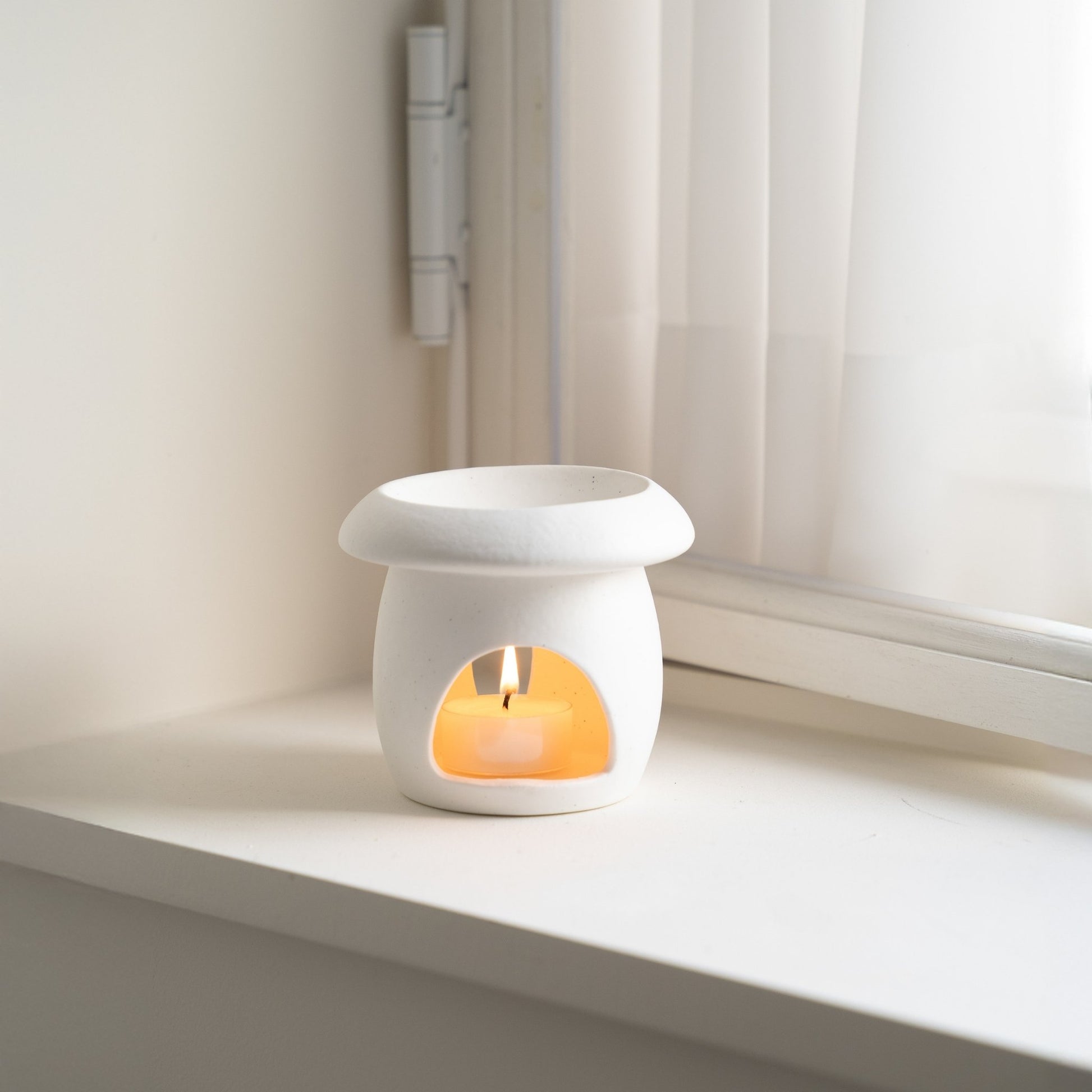 창가 하얀 창틀 위에 놓인 화이트 머쉬룸 오일버너와 안에서 타고 있는 티라이트 캔들 사진
