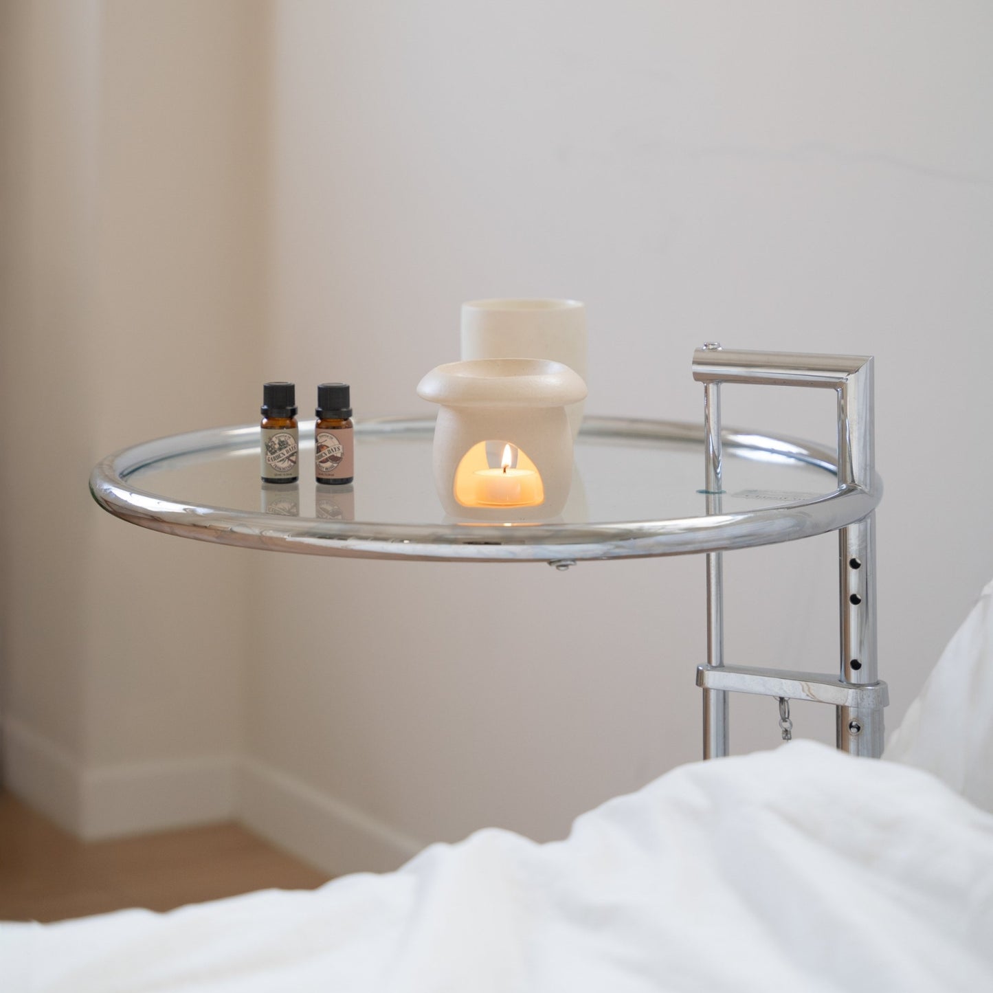 침대 옆 유리 사이드테이블 위에 놓인 베이지 색 머쉬룸 오일버너와 티라이트 캔들, 가든데이즈 에센셜오일 병 두 개가 함께 연출된 사진
