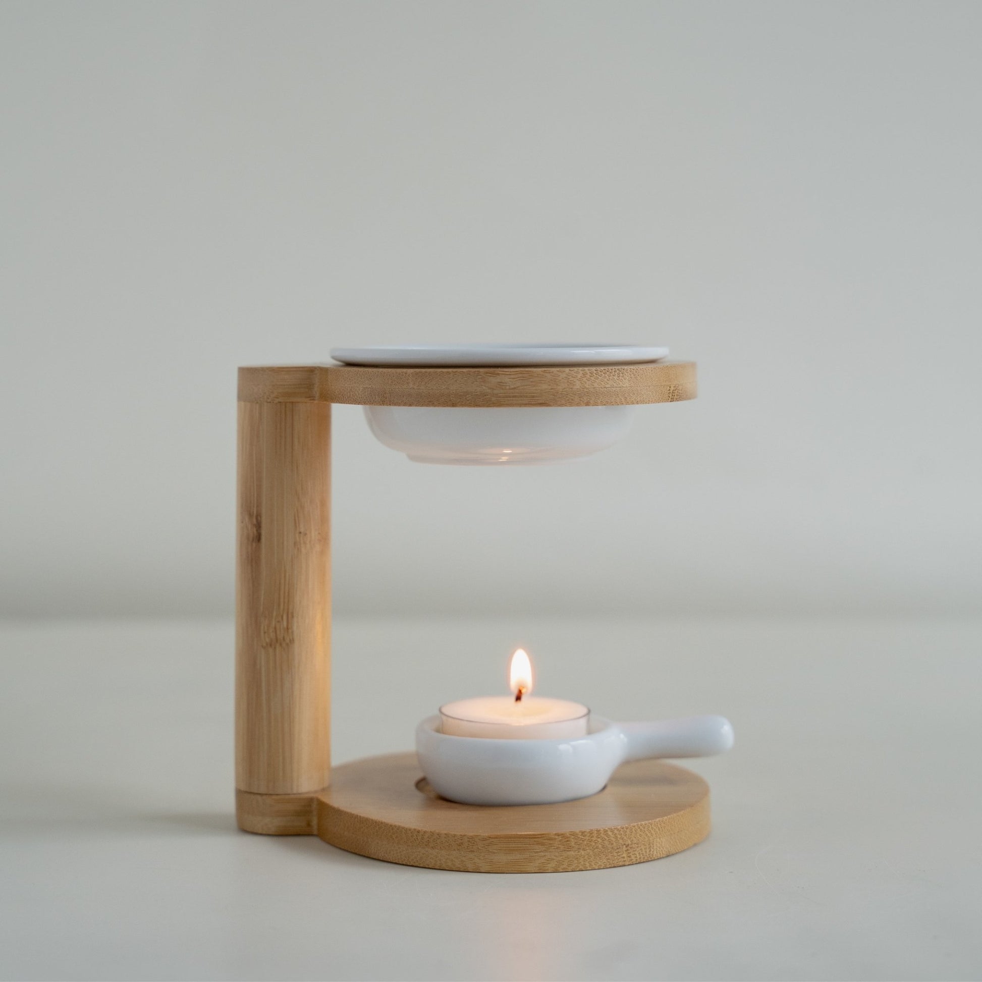 화이트 배경 위 대나무 구조의 우드 오일버너와 상단의 화이트 세라믹 접시, 아래에서 불이 켜진 티라이트 캔들이 보이는 정면 제품 사진