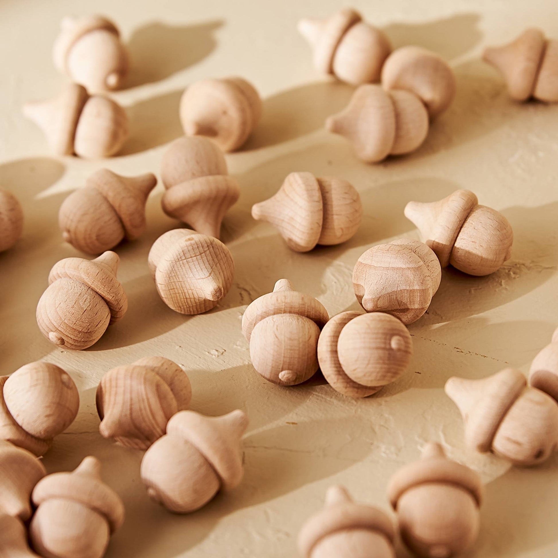 따뜻한 조명 아래 바닥에 흩어지듯 놓인 너도밤나무 도토리 브리즈볼 여러 개를 가까이에서 담은 클로즈업 제품 사진