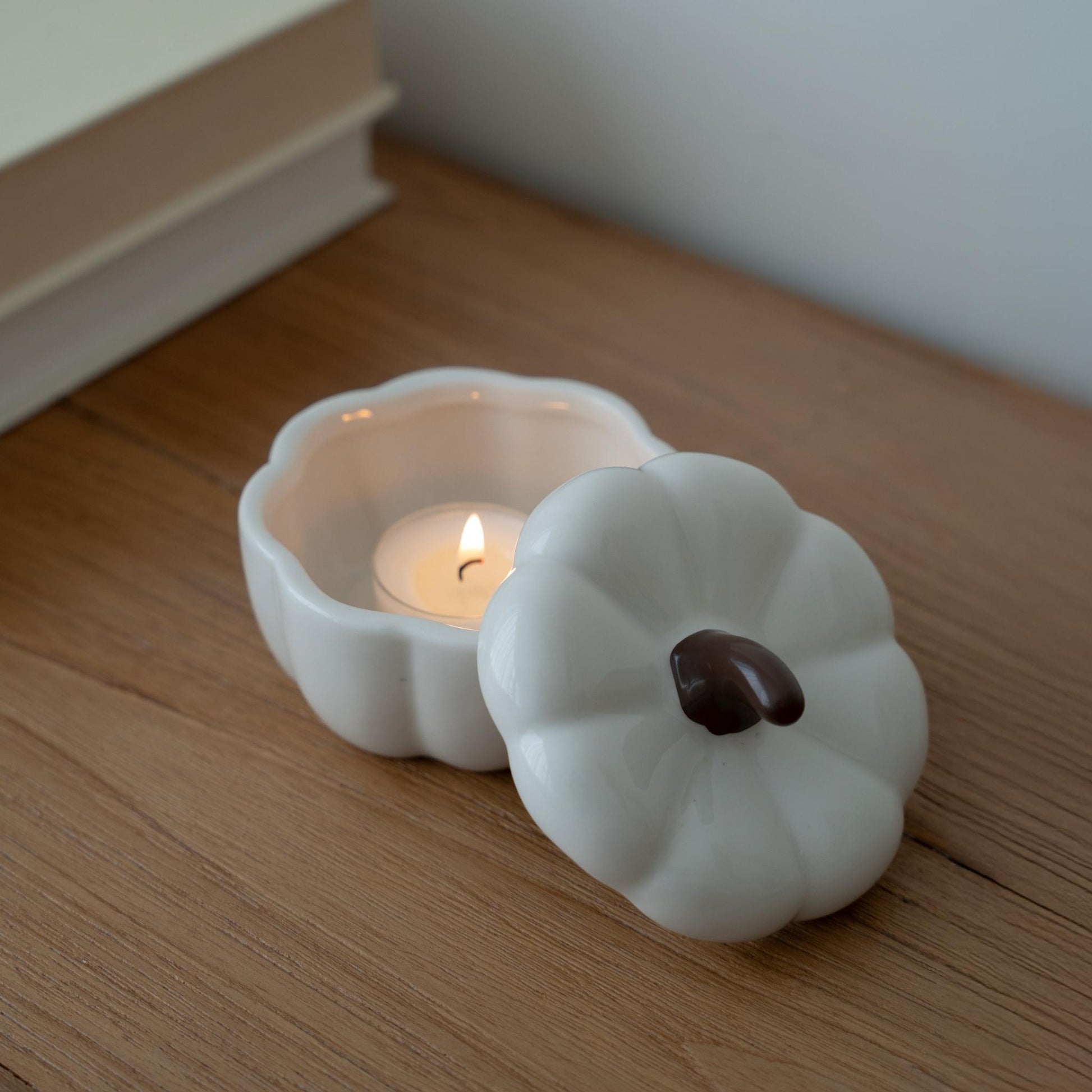  나무 선반 위에 놓인 흰색 호박 모양 캔들 홀더와 안에서 은은하게 켜진 티라이트 캔들이 보이는 미니멀 인테리어 사진