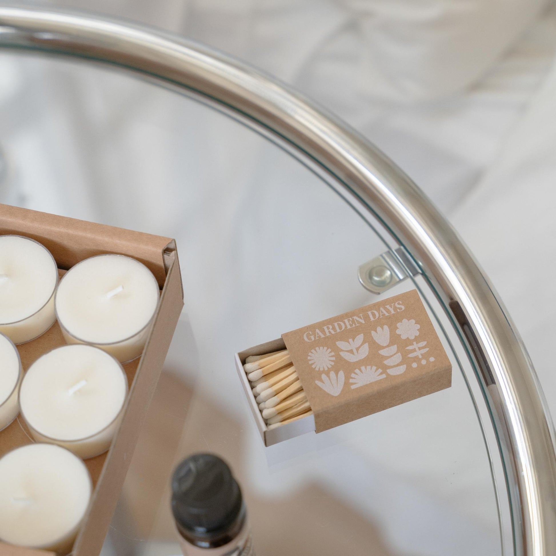 메탈 트레이 위에 놓인 소이 티라이트 캔들 옆으로, 사용 방법 아이콘이 인쇄된 가든데이즈 성냥 상자를 클로즈업한 라운드 오일버너 선물세트 구성품 사진