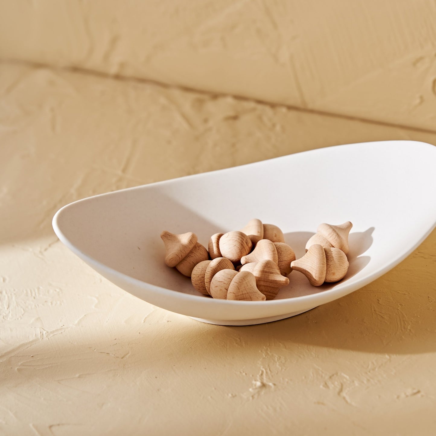 베이지 톤 배경 위 타원형 화이트 접시 안에 너도밤나무로 깎은 도토리 모양 자연발향우드, 도토리 브리즈볼 여러 개가 담긴 메인 연출 사진