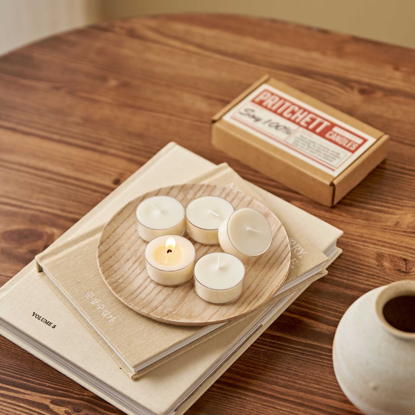 책 위 트레이에 올려진 소이 티라이트 캔들 6개와 옆에 놓인 6개입 작은 상자가 보이는 테이블 연출 사진