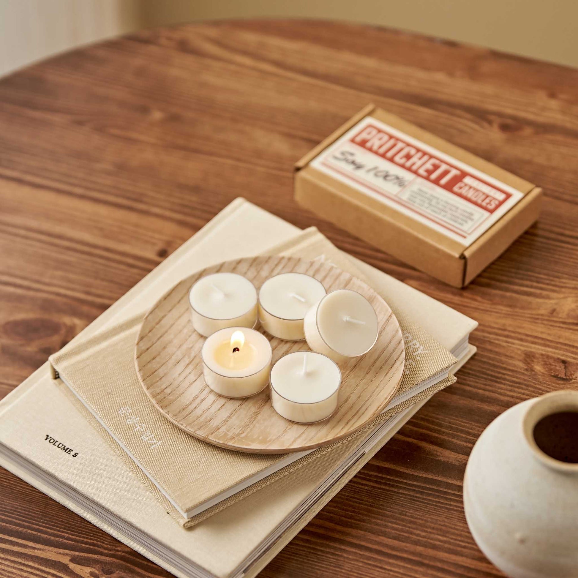 책 위 트레이에 올려진 소이 티라이트 캔들 6개와 옆에 놓인 6개입 작은 상자가 보이는 테이블 연출 사진