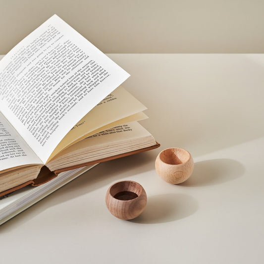 열어 둔 책 앞 크림색 상판 위에 나란히 놓인 밝은 원목과 진한 원목으로 만든 반구형 우드 발향제품 에그 브리즈볼 두 개가 보이는 메인 사진