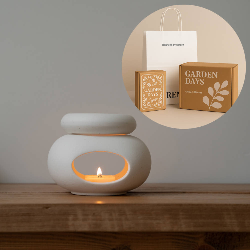 나무 테이블 위에서 티라이트 캔들이 켜진 하얀 조약돌 도자기 오일버너가 보이고, 상단 원형 인셋 이미지에는 쇼핑백과 선물박스, 에센셜오일·소이캔들·성냥이 포함된 조약돌 오일버너 선물세트 패키지가 함께 보이는 사진