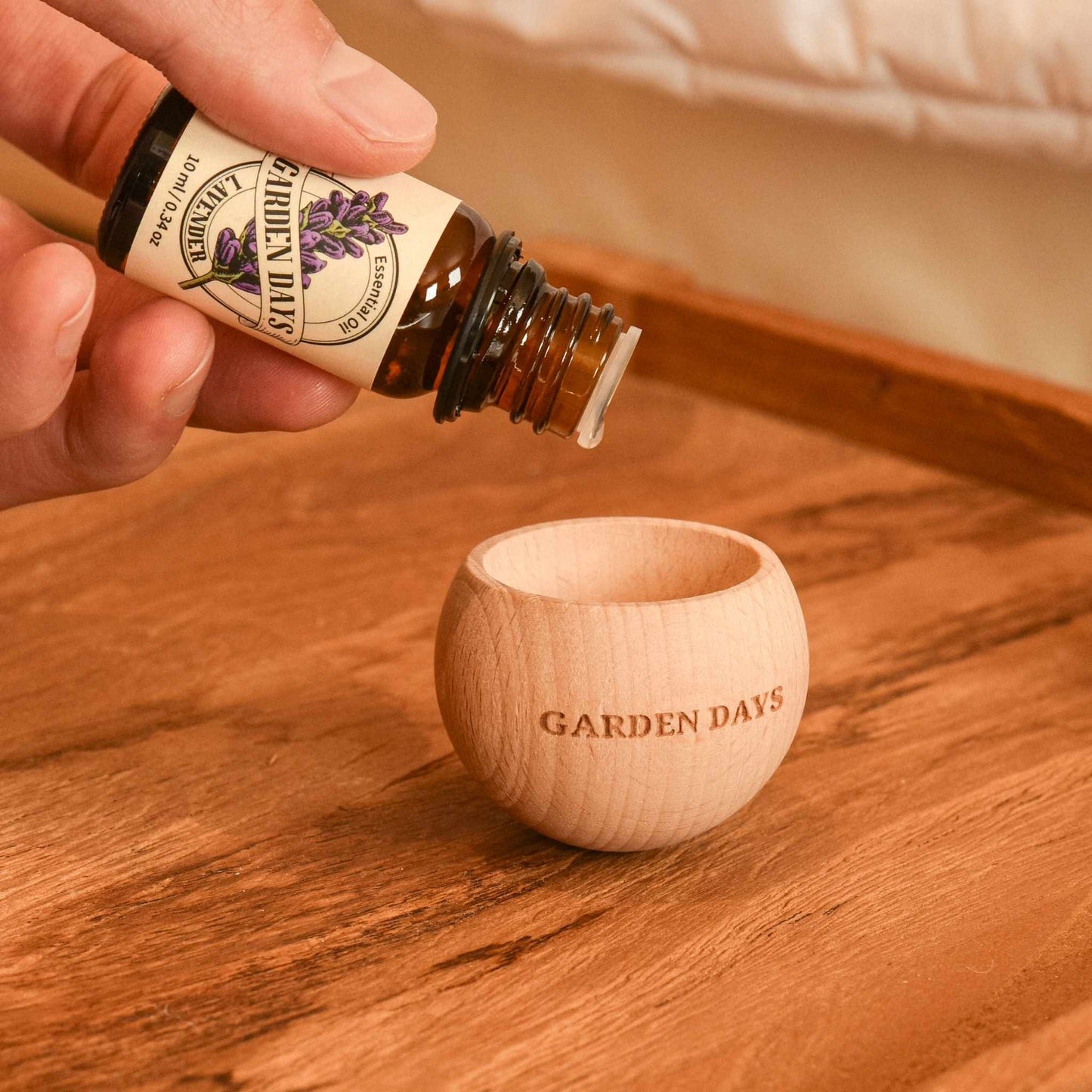 우드 바닥 위 에그 브리즈볼 우드 발향 제품 안으로 가든데이즈 천연 100% 에센셜오일을 떨어뜨리는 손이 보이는 사용 방법 연출 사진