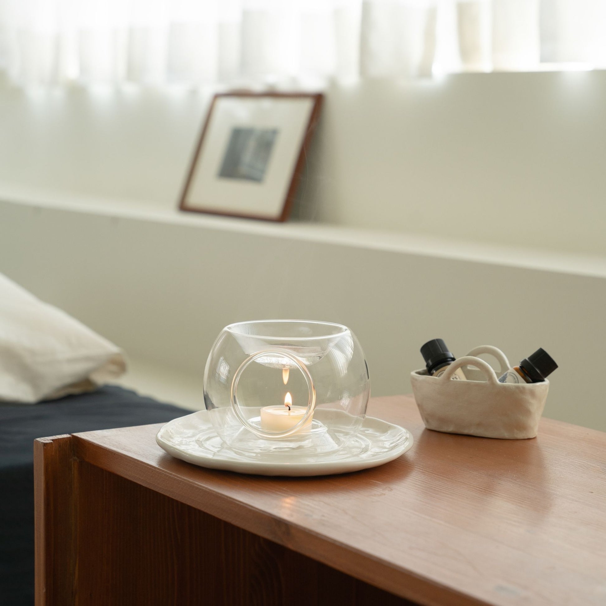 화이트 선반 위에 단독으로 놓인 투명 유리 티라이트 홀더와 작은 티라이트 캔들이 보이는 심플한 인테리어 사진