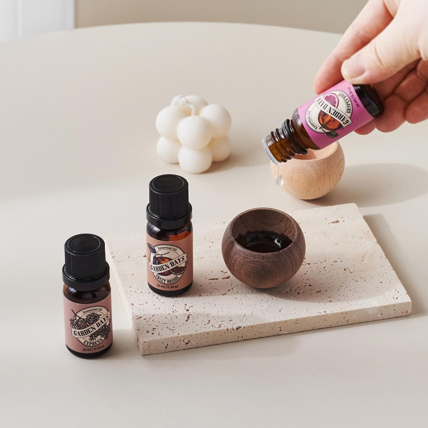 테라조 트레이 위 진한 색 에그 브리즈볼에 에센셜오일을 떨어뜨리는 손과 옆에 세워진 가든데이즈 에센셜오일 병들이 보이는 사용 방법 연출 사진