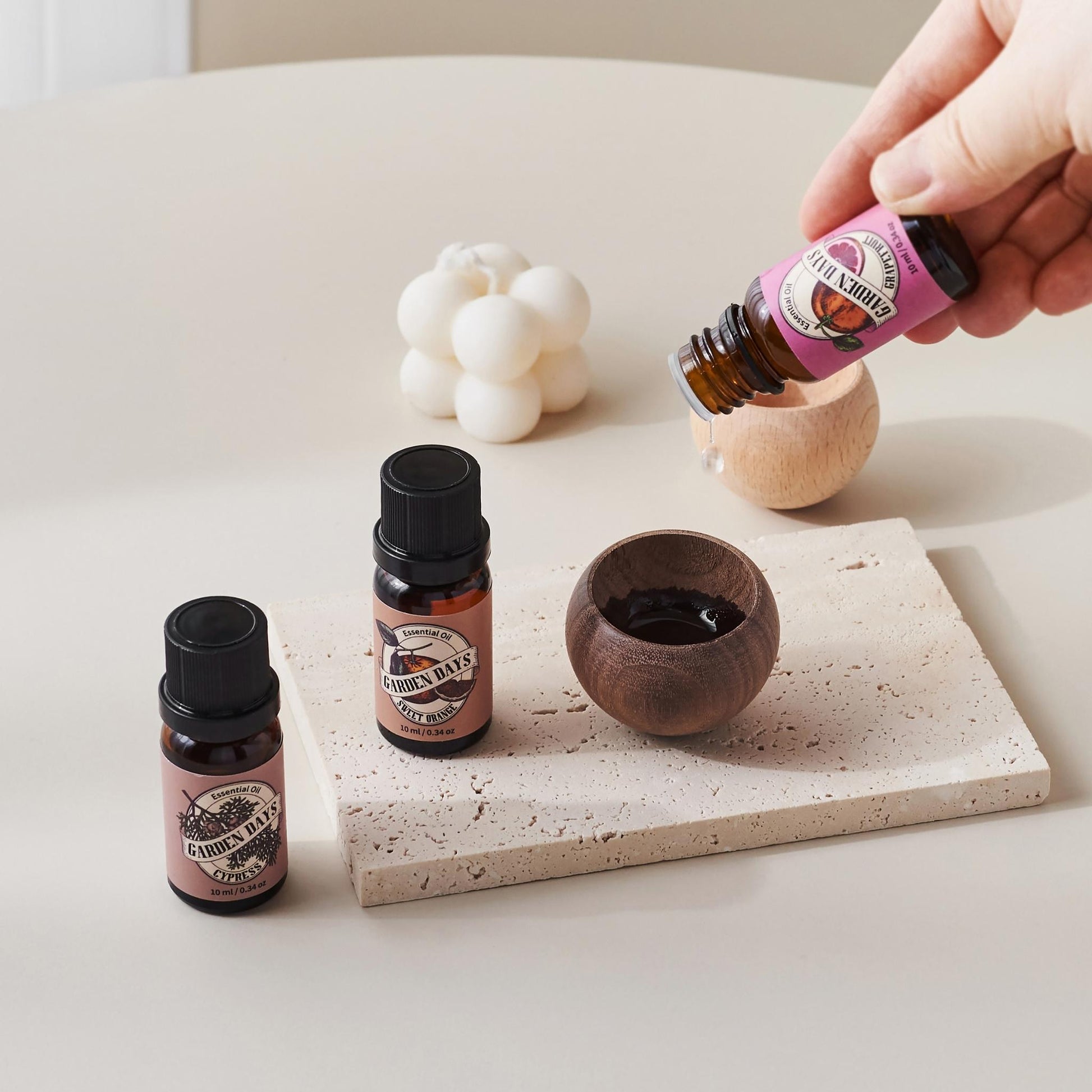 테라조 트레이 위 진한 색 에그 브리즈볼에 에센셜오일을 떨어뜨리는 손과 옆에 세워진 가든데이즈 에센셜오일 병들이 보이는 사용 방법 연출 사진