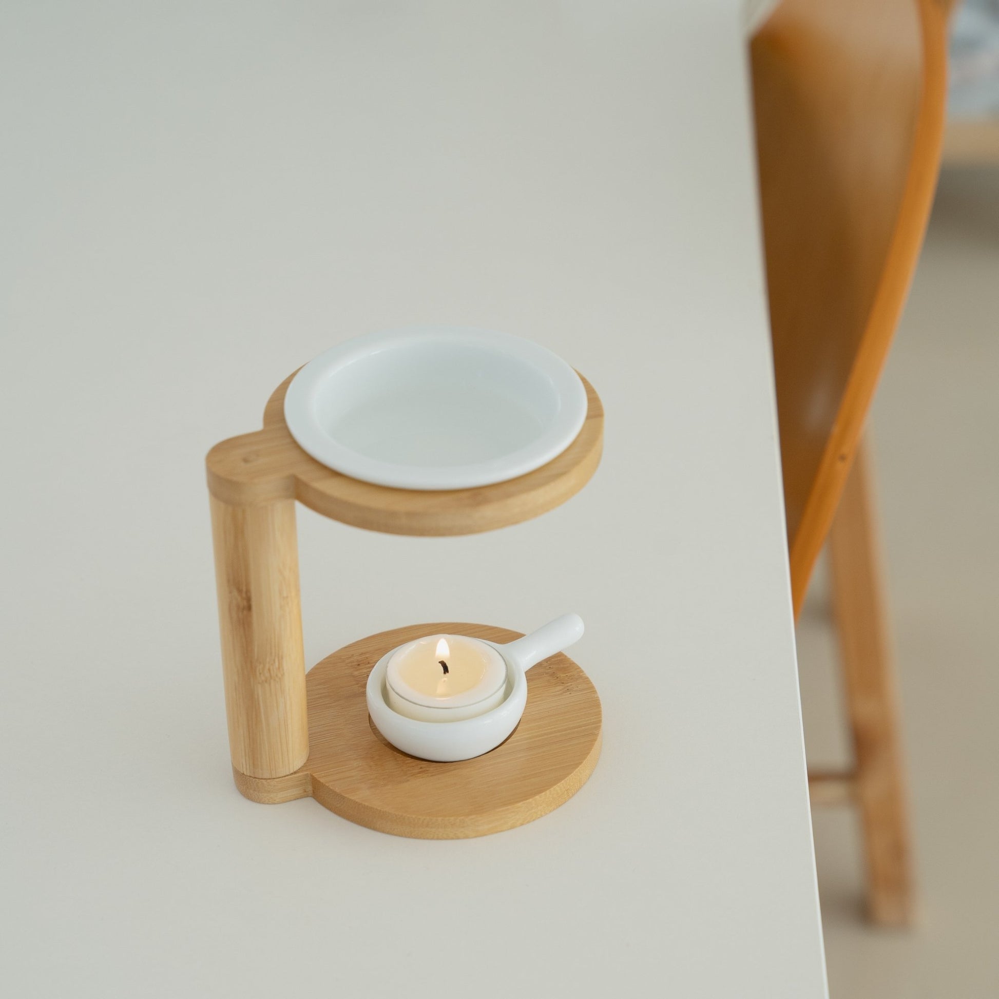 화이트 테이블 위 의자 옆에 놓인 우드 오일버너와 화이트 세라믹 접시, 아래 불이 켜진 티라이트 캔들을 위에서 담은 연출 사진