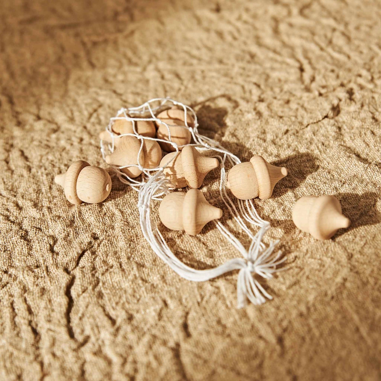 거친 질감의 베이지 표면 위에 도토리 브리즈볼과 라탄 장식, 식물 오브제가 함께 놓인 내추럴 무드 연출 사진