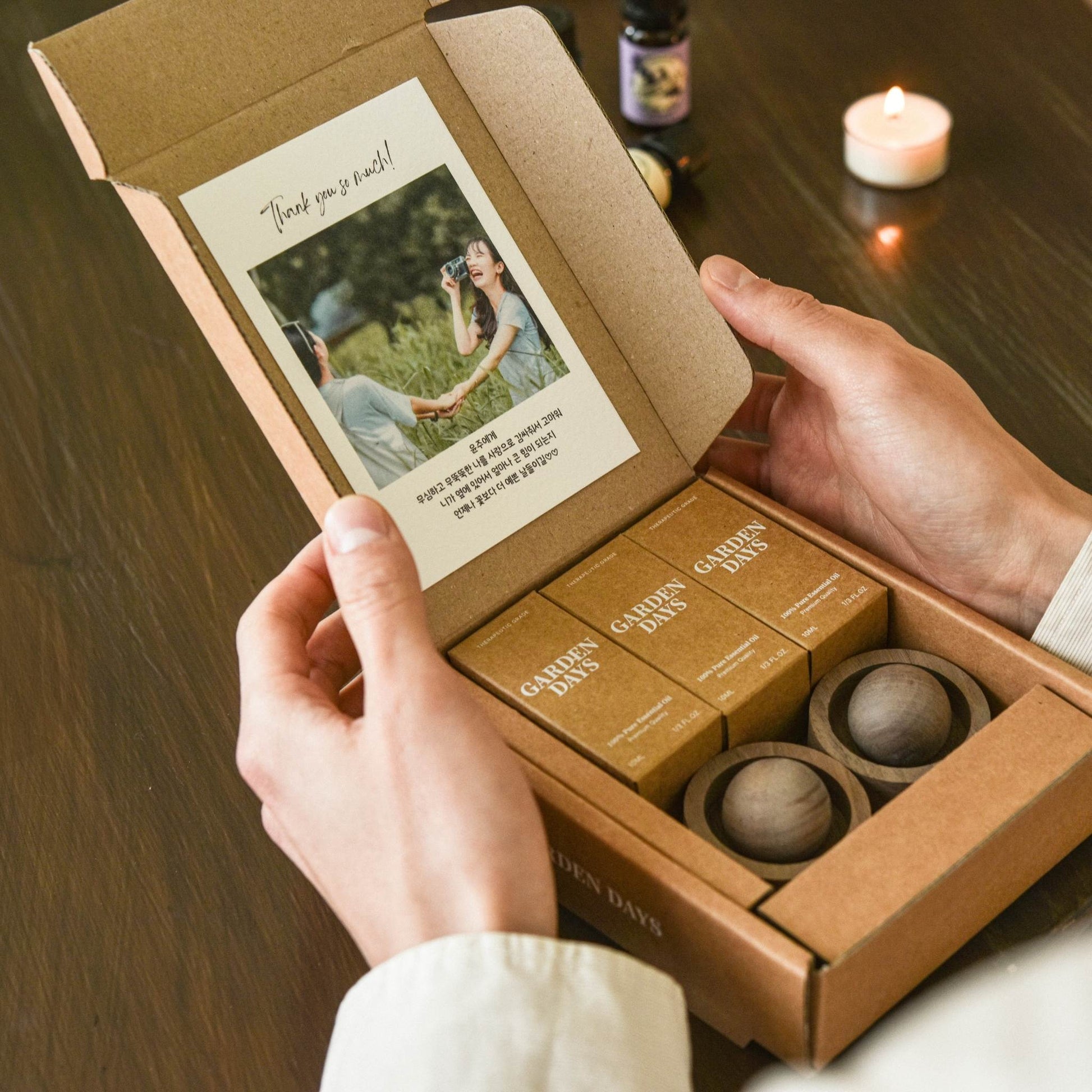 맞춤 인쇄 카드가 붙어 있는 호두 브리즈볼 선물세트 박스를 두 손으로 열어 보는 모습, 안에 호두 브리즈볼 2개와 에센셜오일 3개가 가지런히 담긴 사진