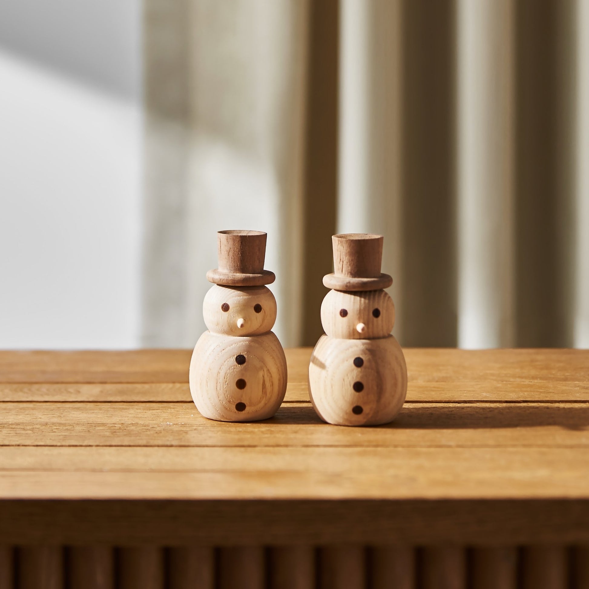 커튼이 드리운 창가 난간 위에 나란히 세워진 우드 스노우맨 디퓨저 두 개가 보이는 연출 사진