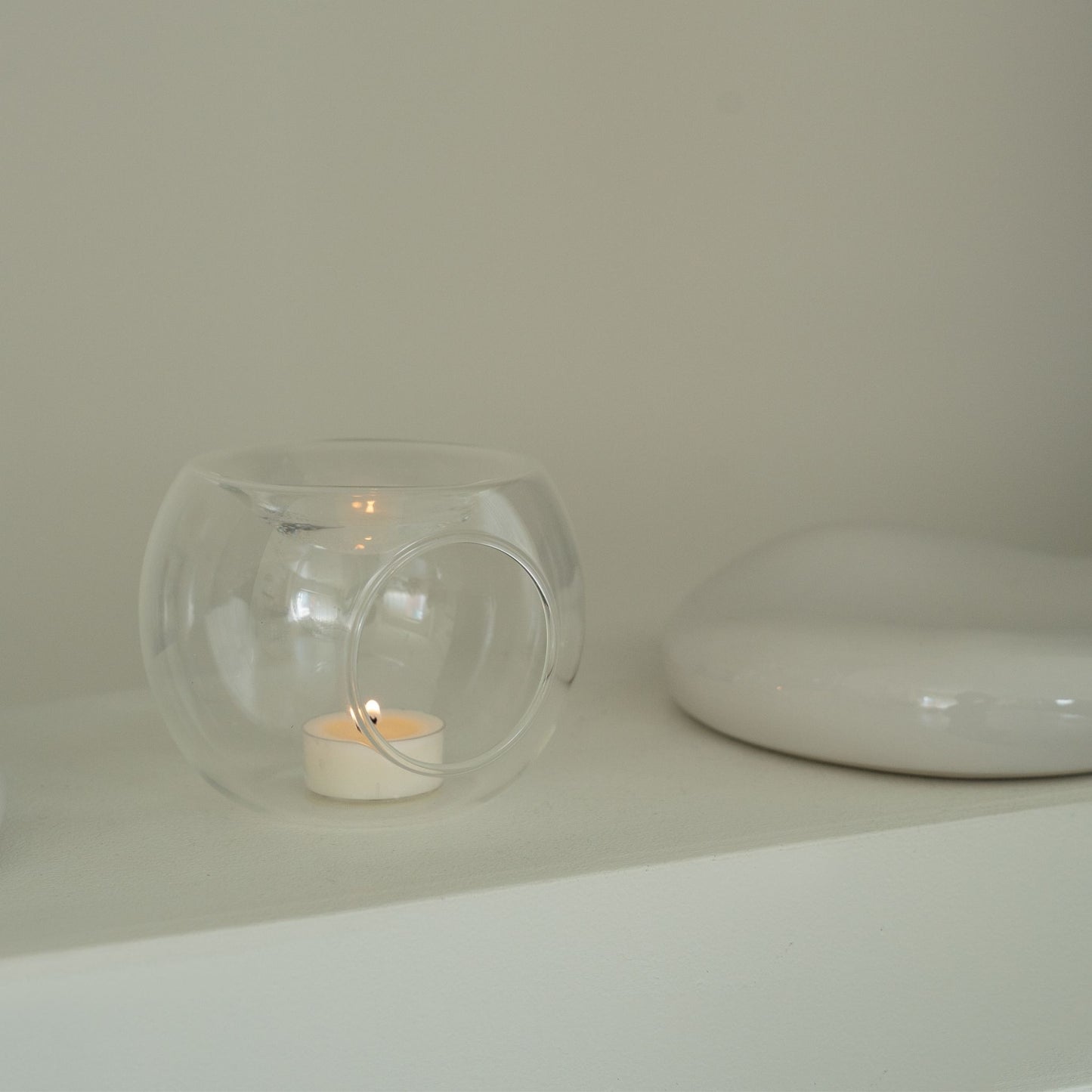 블랙 테이블 위 책 더미와 블랙 화병 옆에 놓인 투명 유리 티라이트 홀더와 은은한 불빛의 티라이트 캔들이 보이는 연출 사진