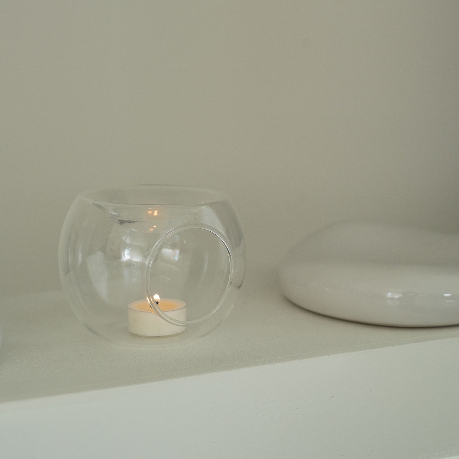 블랙 테이블 위 책 더미와 블랙 화병 옆에 놓인 투명 유리 티라이트 홀더와 은은한 불빛의 티라이트 캔들이 보이는 연출 사진