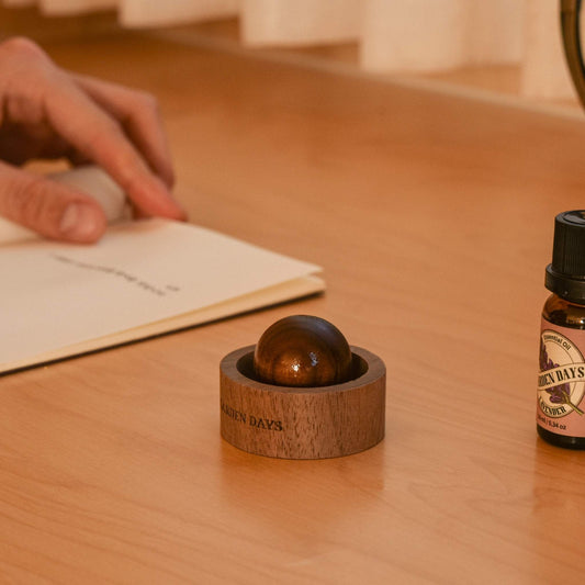 나무 책상 위 책 옆에 놓인 호두나무 우드 발향제품 호두 브리즈볼과 옆에 세워둔 가든데이즈 에센셜오일 병이 보이는 메인 연출 사진