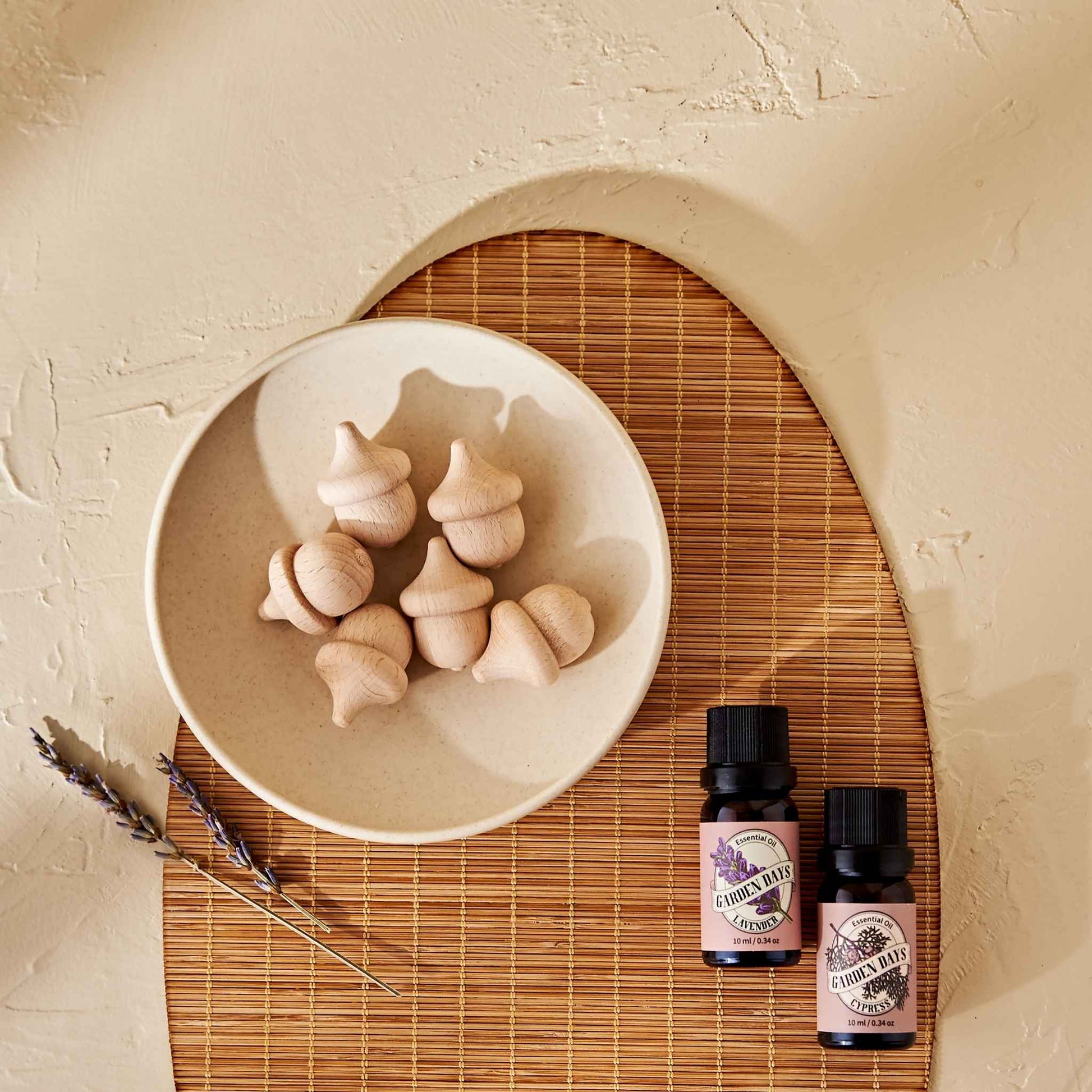 라탄 매트 위 화이트 볼에 담긴 도토리 브리즈볼과 옆에 놓인 가든데이즈 에센셜오일 병 두 개가 함께 보이는 사용 연출 사진