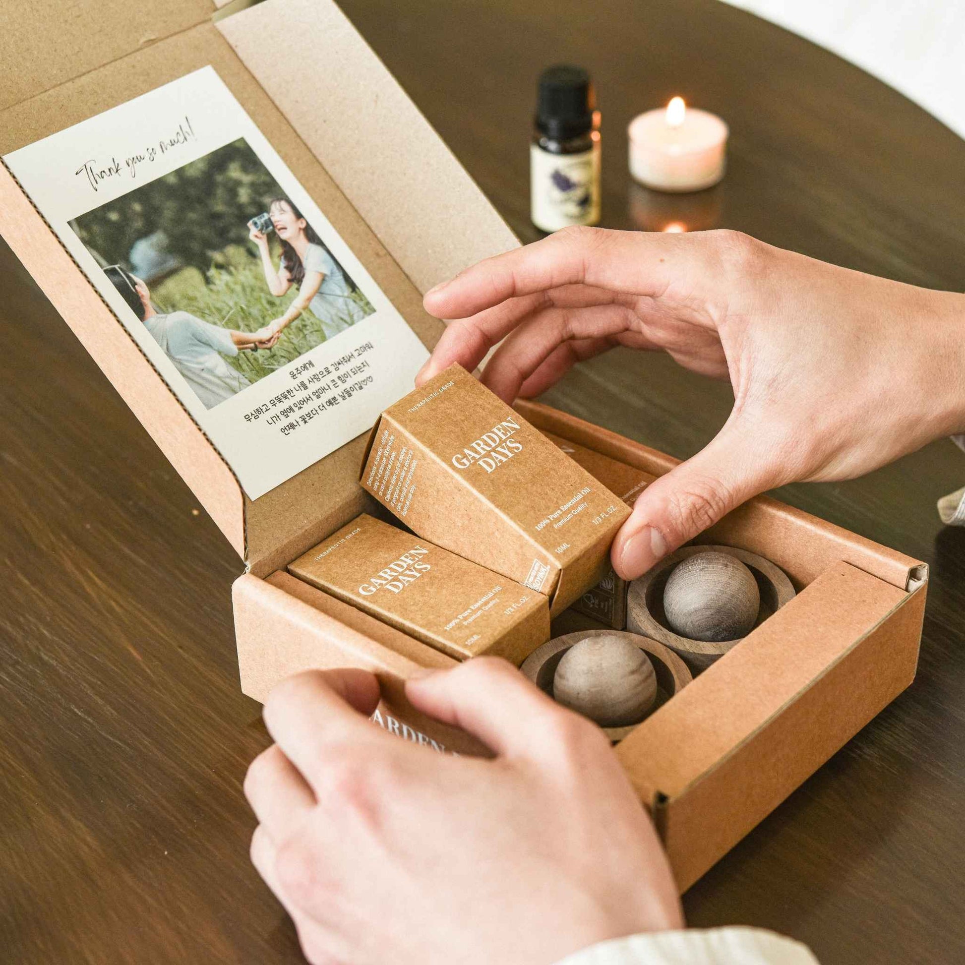 테이블 위에서 맞춤카드가 붙은 호두 브리즈볼 선물세트 박스를 열어 제품 구성을 확인하는 손이 보이는 사진