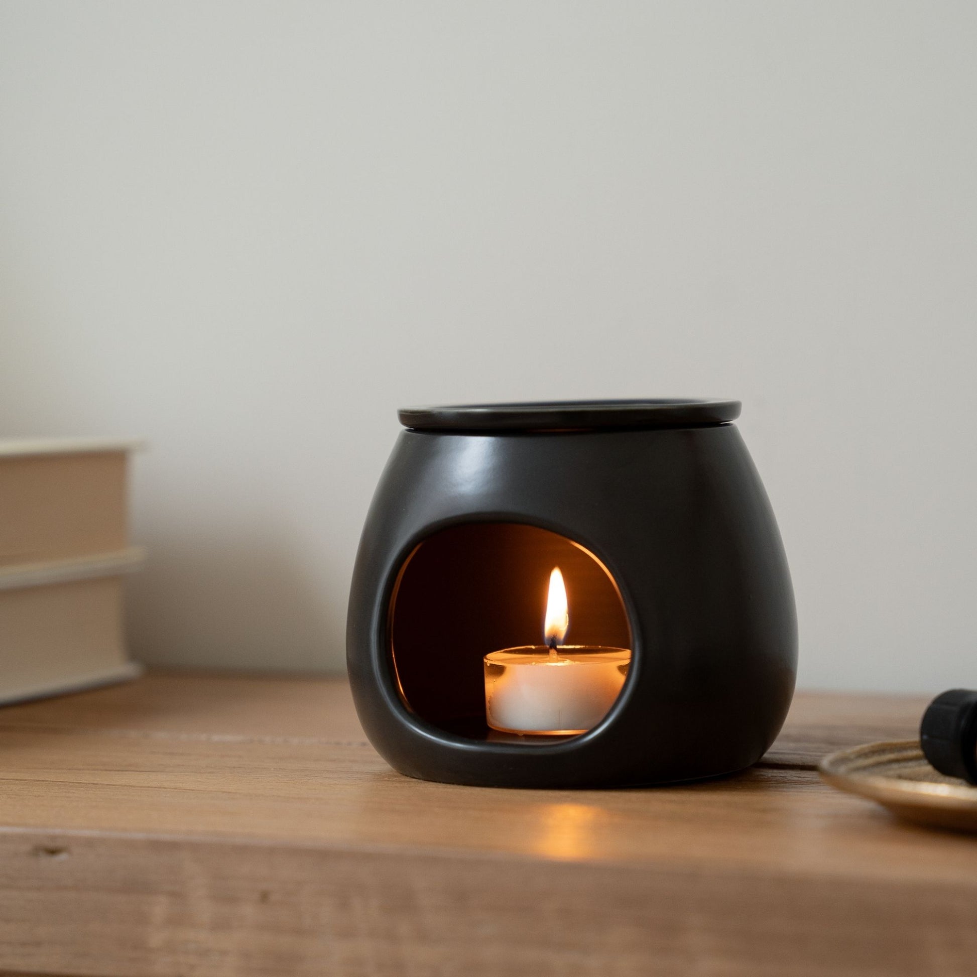 테이블 위에 블랙 세라믹 오일버너와 안에서 밝게 켜진 티라이트 캔들이 보이는 제품 연출 사진