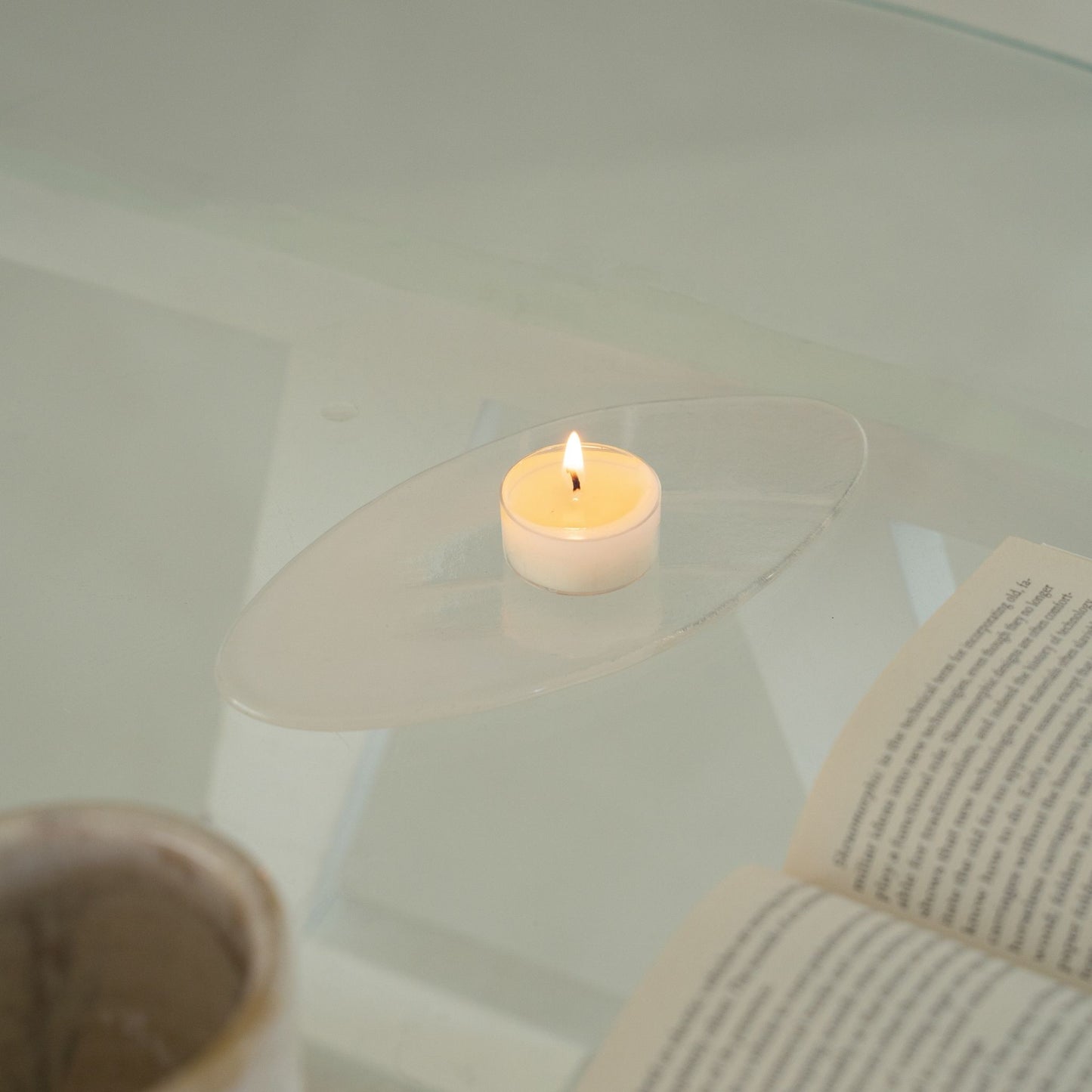 투명한 받침 접시 위에서 따뜻한 불빛을 내고 있는 소이 티라이트 캔들을 가까이에서 담은 연출 사진