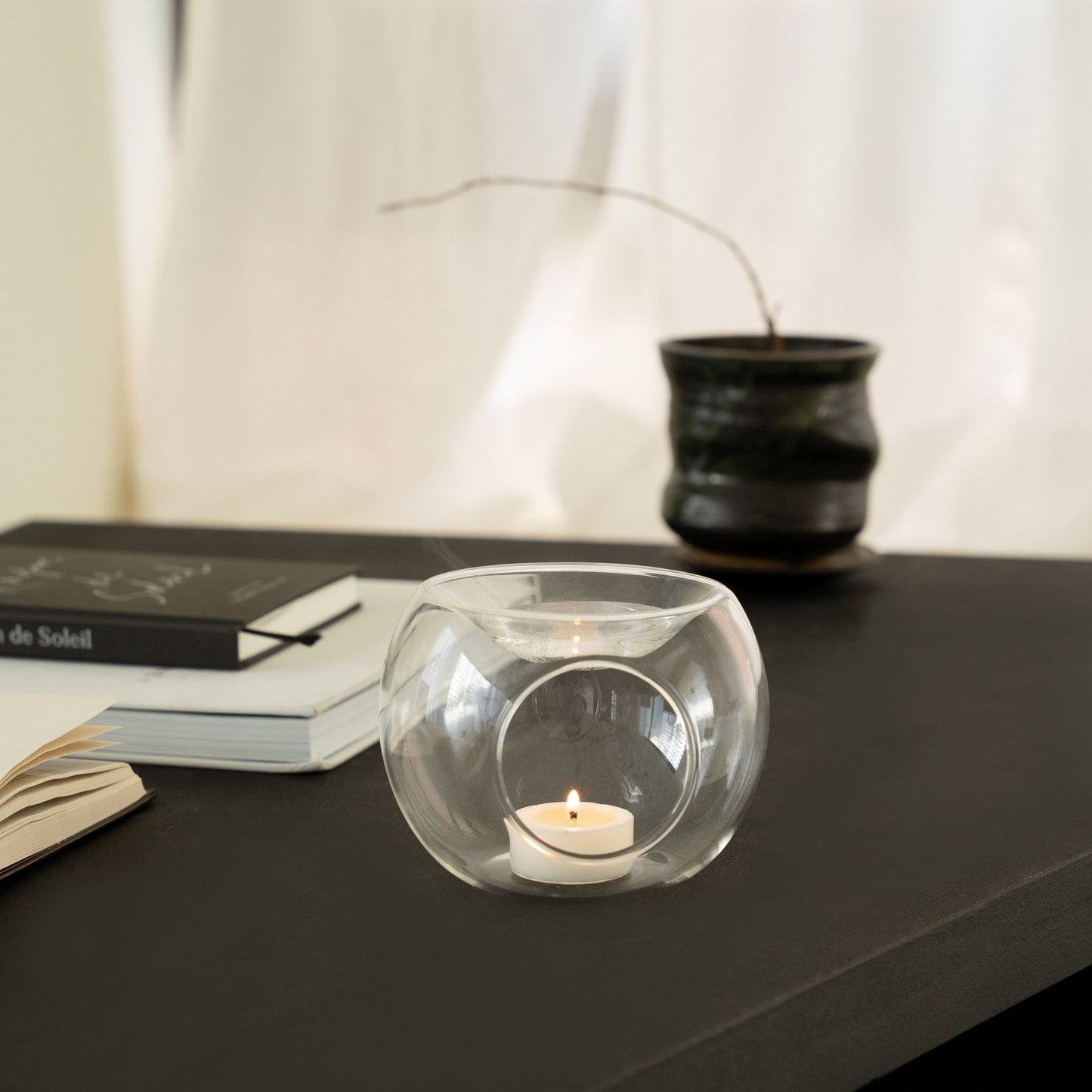 사이드테이블 위에 놓인 투명 유리 티라이트 홀더와 안에서 켜진 티라이트 캔들을 살짝 비껴서 담은 인테리어 연출 사진