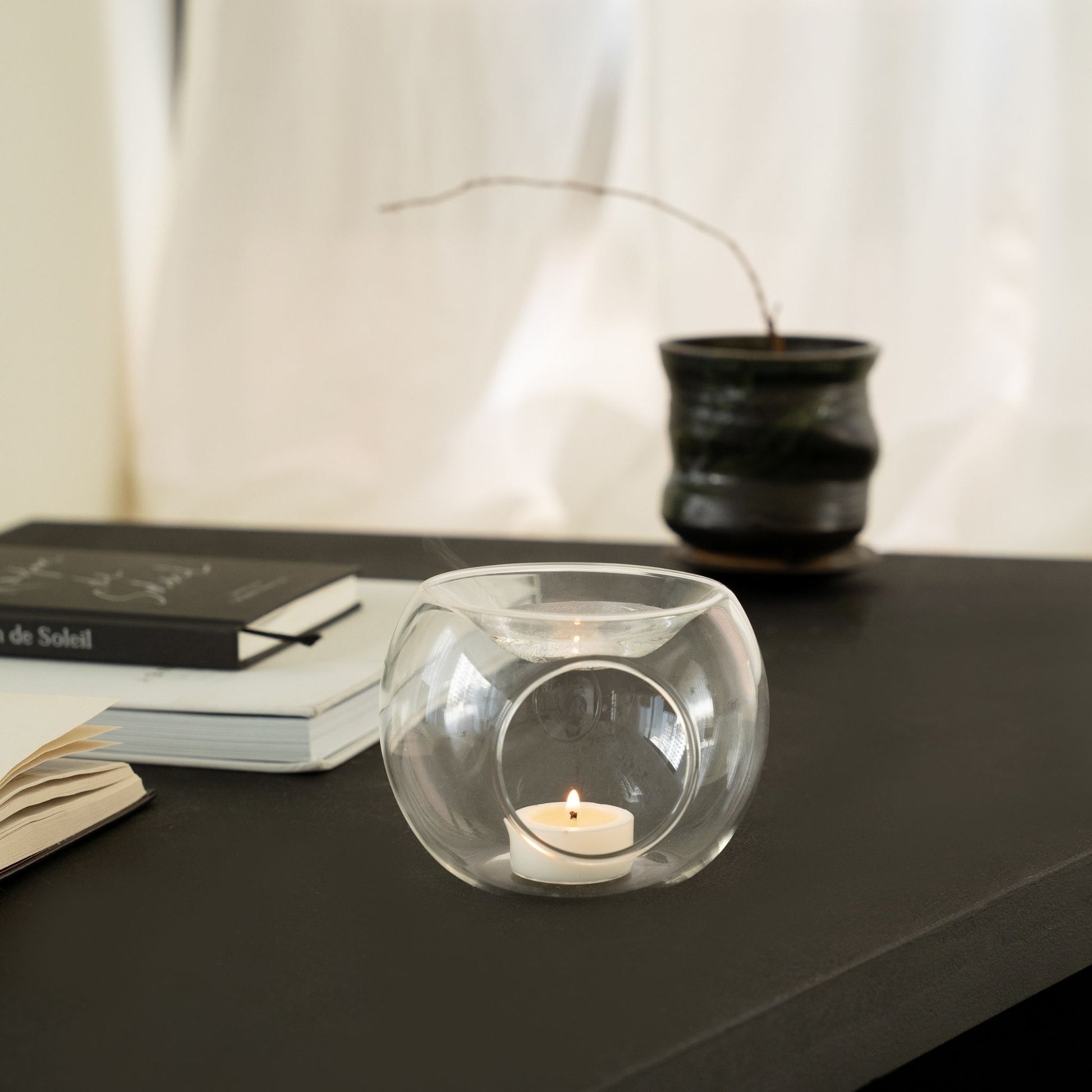 사이드테이블 위에 놓인 투명 유리 티라이트 홀더와 안에서 켜진 티라이트 캔들을 살짝 비껴서 담은 인테리어 연출 사진