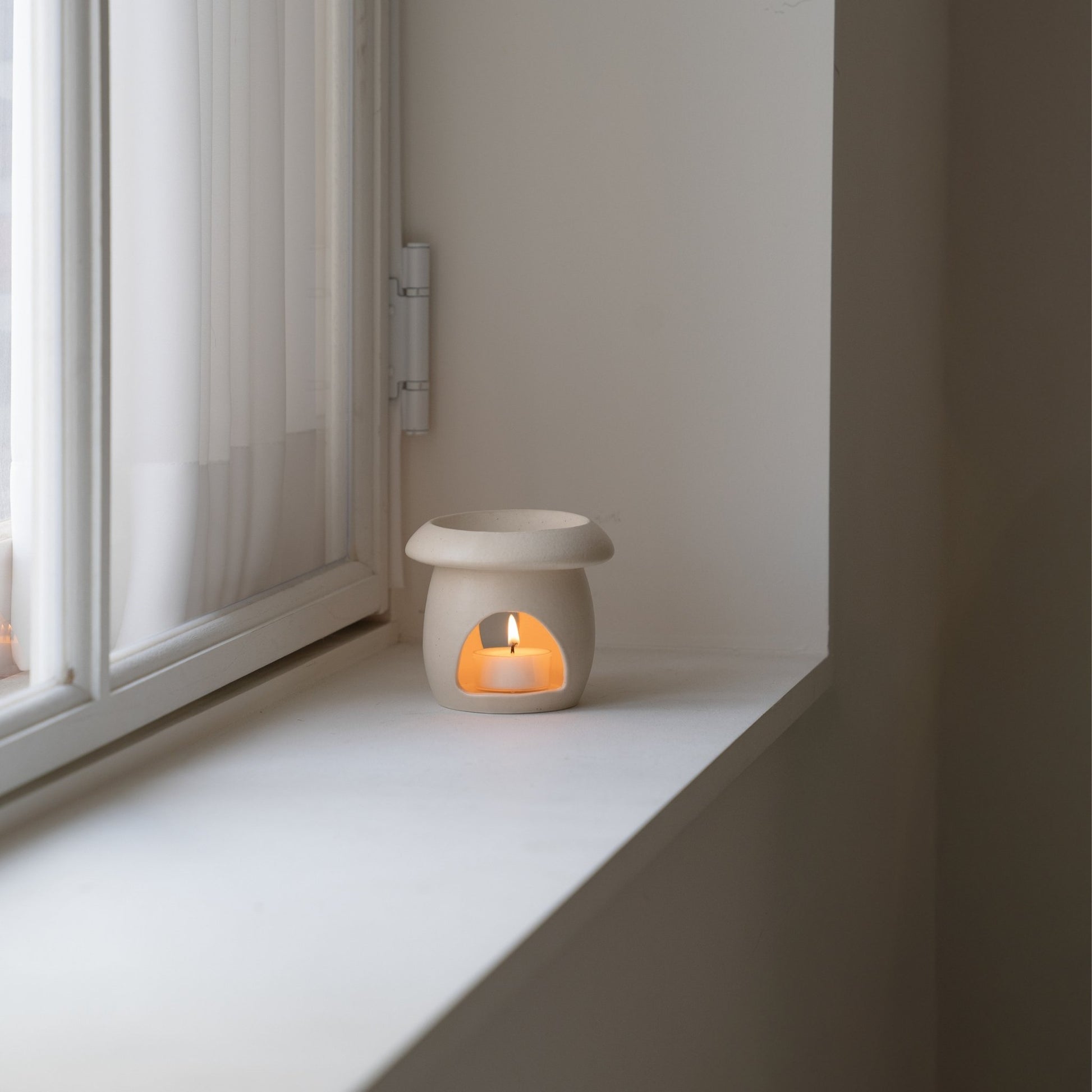 창가 하얀 창틀 위에 놓인 베이지 색 머쉬룸 오일버너와 안에서 켜진 티라이트 캔들 사진