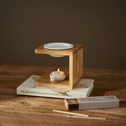 책 위에 올려진 우드 오일버너와 아래쪽 불이 켜진 티라이트 캔들, 옆에 놓인 성냥갑이 보이는 따뜻한 분위기의 연출 사진