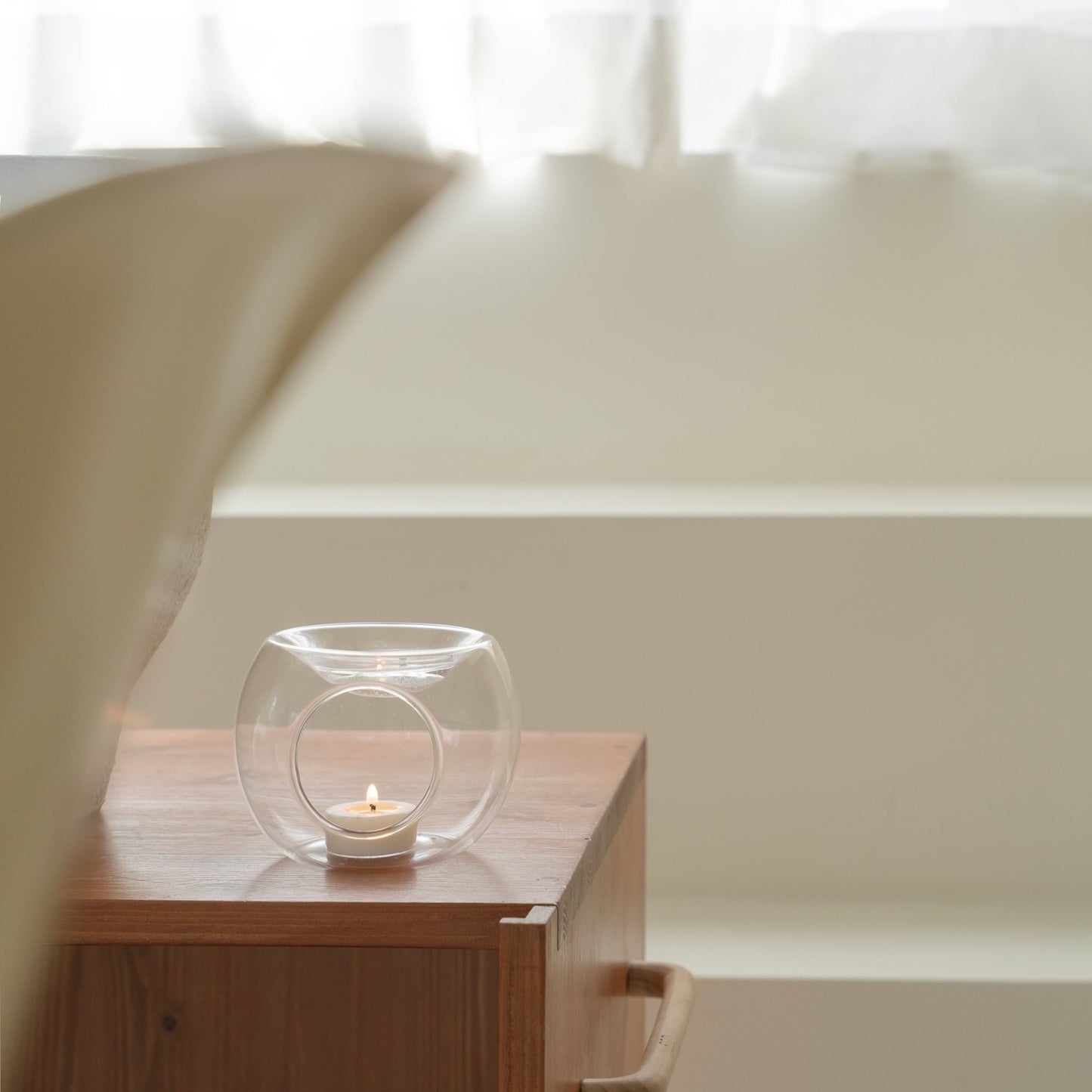 원목 서랍장 위에 놓인 투명 유리 티라이트 홀더와 안에서 켜진 티라이트 캔들을 담은 인테리어 연출 사진